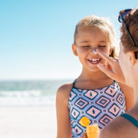 Mother applying suntan lotion on daughter face