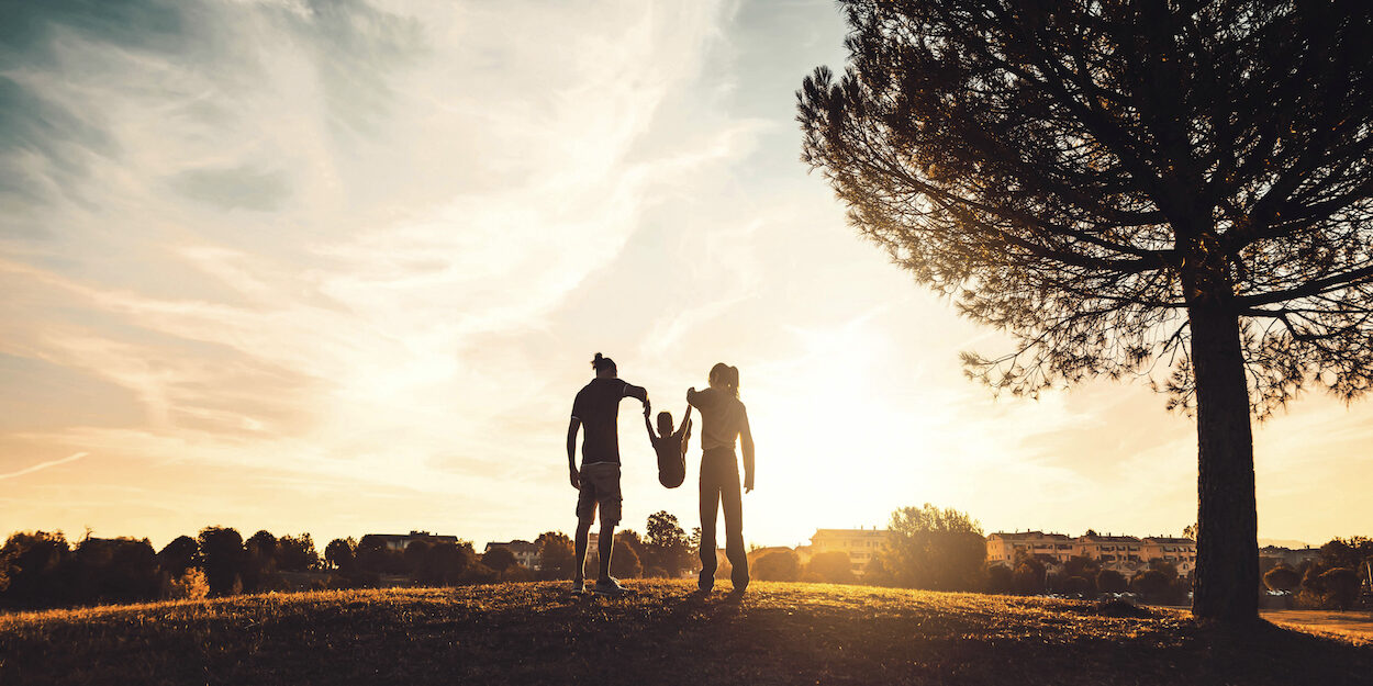 Silhouette of happy family walking in the meadow at sunset - Mother, father and child son having fun outdoors enjoying time together - Family, love, mental health and happy lifestyle concept